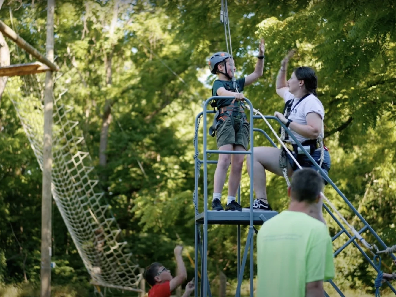 A Camp Accomplish camper and a Camp Accomplish counselor high fiving on the ropes course.